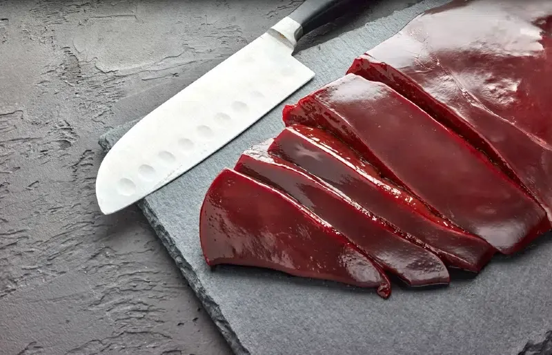 sliced beef liver with knife on black stone cutting board
