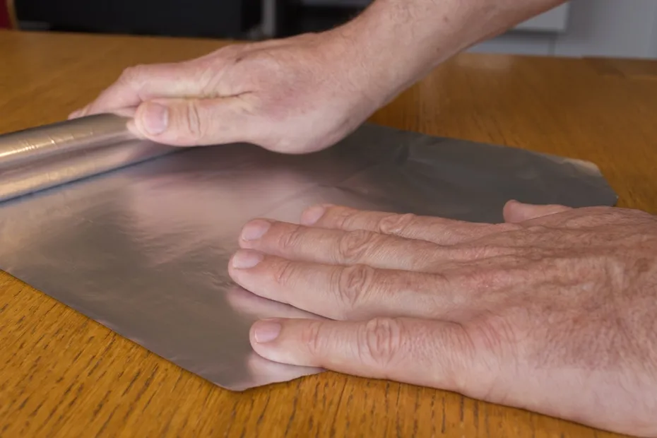 Men hands roll off the aluminum foil for household use on a wooden surface