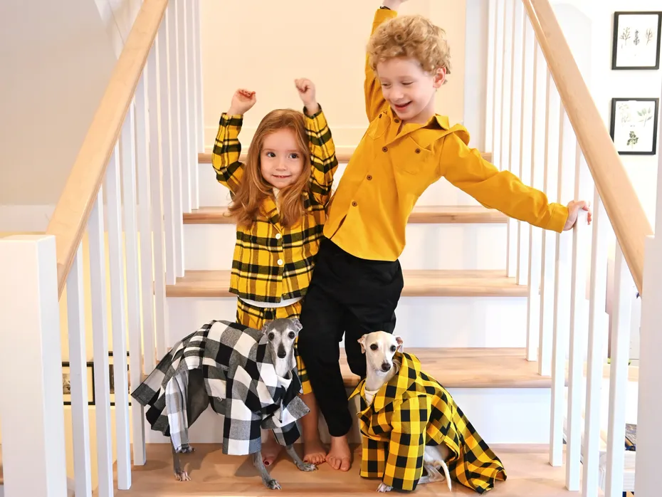 Two children and two Italian greyhounds in plaid outfits on a staircase