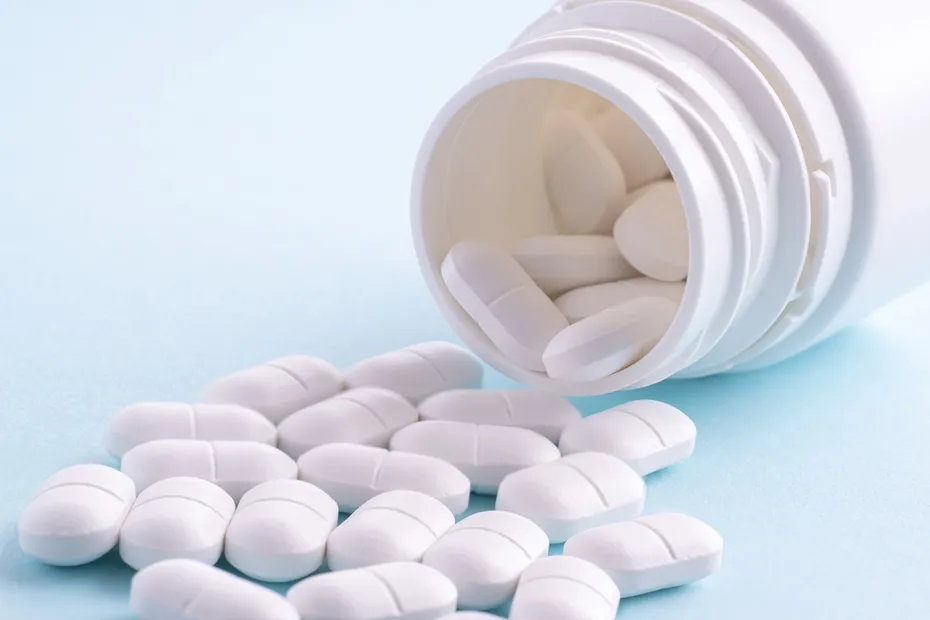 White pills spilling out of pill bottle on white