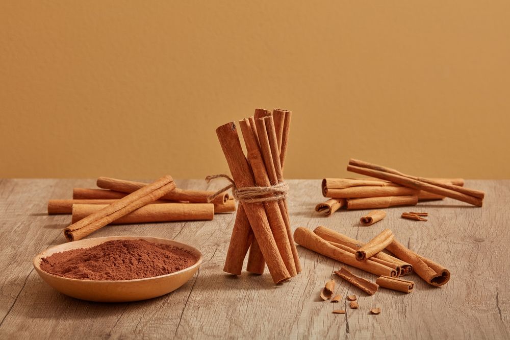 cinnamon sticks are decorated on a wooden table with cinnamon powder placed on a dish