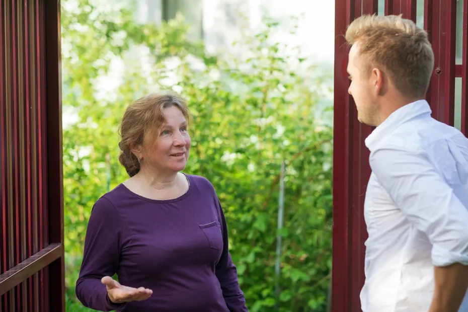 Neighbors discuss the news, standing at the fence or An elderly woman talking with a young man