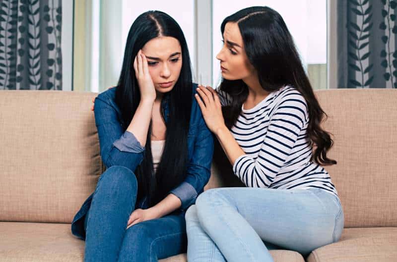 Two women on couch talking, one girl calm down her friend