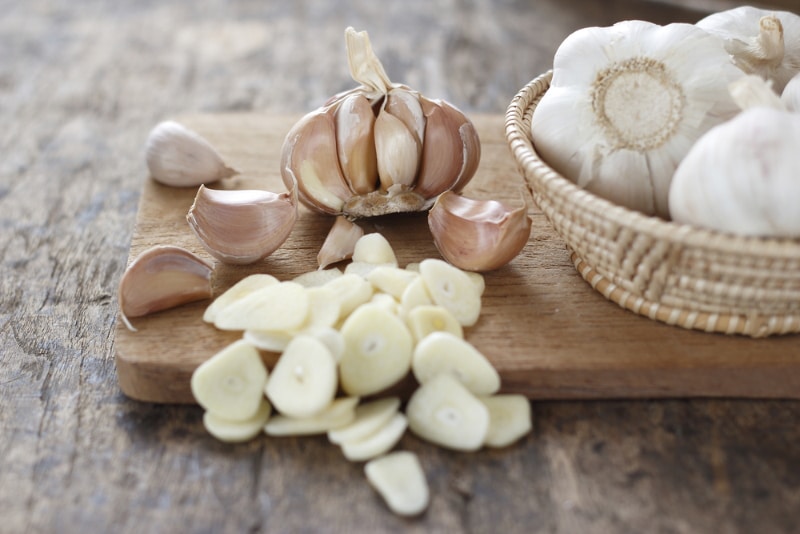 sliced garlic, garlic clove, garlic bulb in wicker basket place on chopping block on vintage wooden background