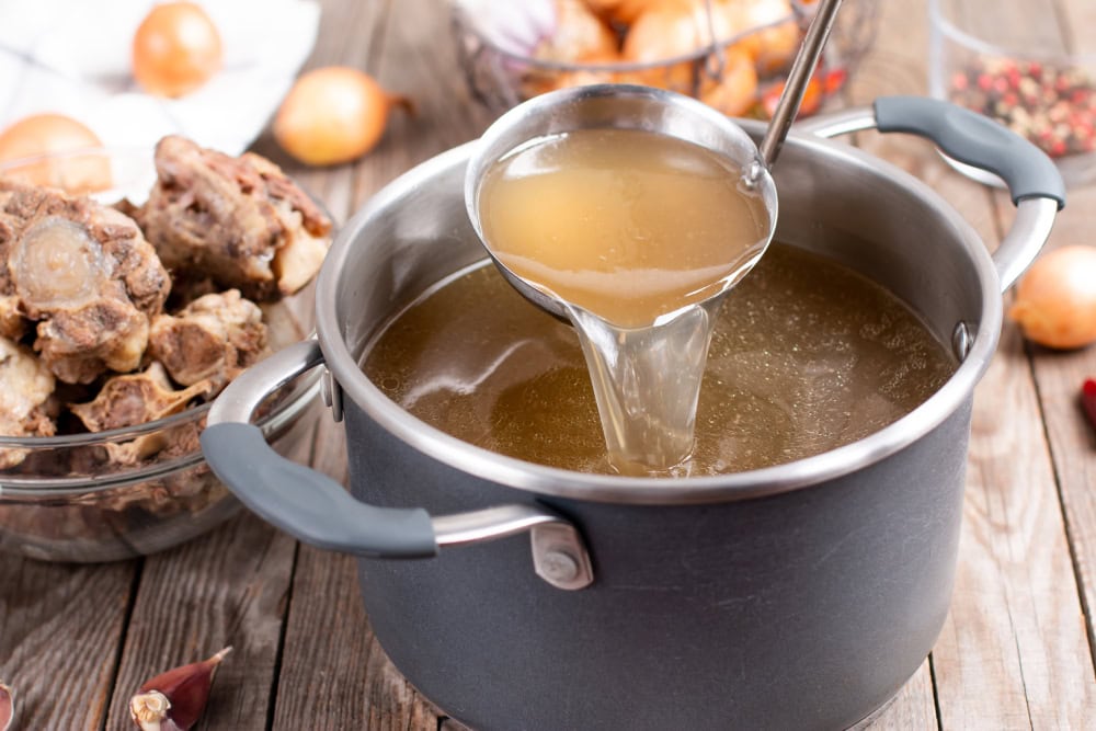 Saucepan with bouillon with a ladle on the table Bone broth