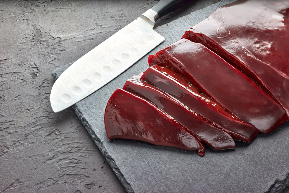 sliced beef liver with knife on black stone cutting board