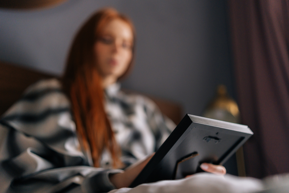 woman lying on bed holding photo in frame and crying or sad looking at picture