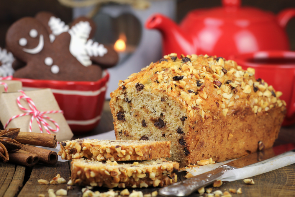 Christmas table setting with a freshly baked sliced festive cake with chocolate and chopped nuts, red teapot, gingerbread cookies