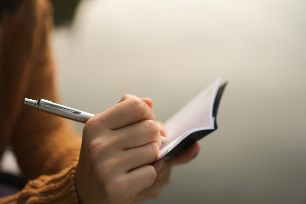 Woman hand writing down in small white memo notebook for take a note