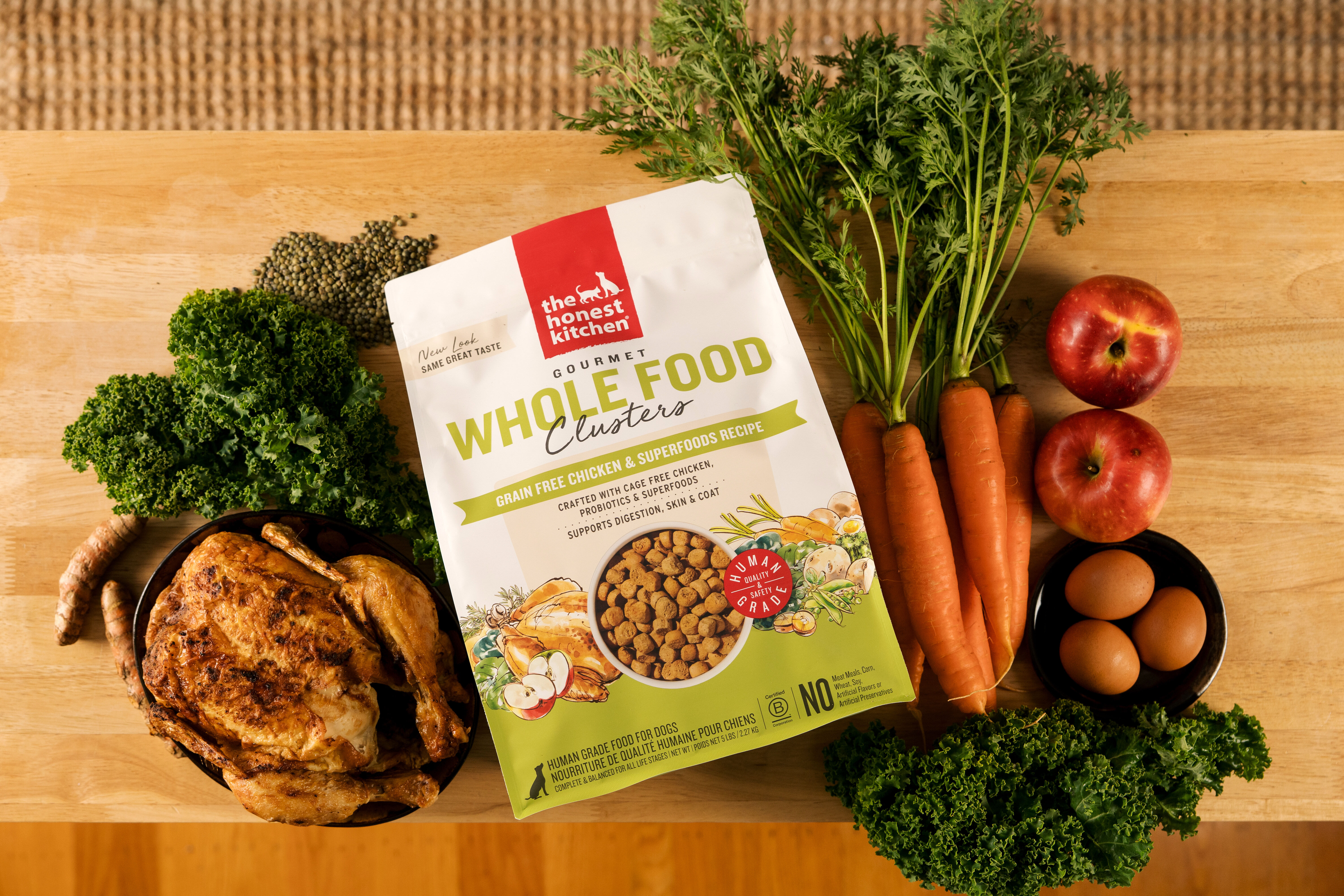 The Honest Kitchen dog food bag surrounded by raw chicken, kale, and carrots