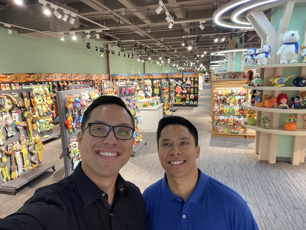 Two men smiling inside a toy store with shelves of pet toys
